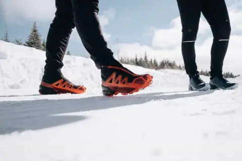 Deux personnes en chaussures de trail, l'une avec des chaussures orange vif, parcourent un sentier enneigé du Haut Giffre.