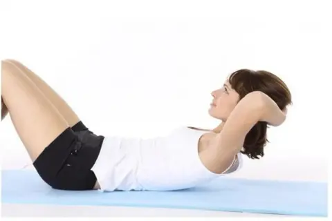 Femme effectuant des abdos hypopressifs sur un tapis bleu.