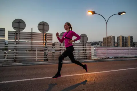 Une femme en tenue de sport rose et noire court sur une route au crépuscule, profitant d'une course de nuit sous les lampadaires.
