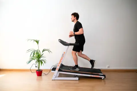 Un homme court sur un tapis de course, suivant un programme d'entraînement. Une plante verte décore la pièce.
