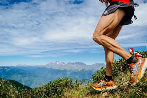 Un coureur en plein entrainement trail, jambes musclées, sur un sentier de montagne avec un panorama spectaculaire.