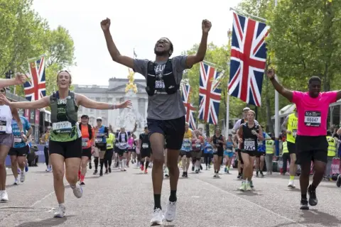 Des coureurs célèbrent leur arrivée au plus grand marathon du monde, drapeaux britanniques en arrière-plan.