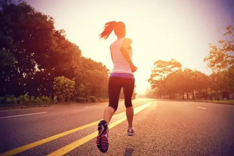 Une coureuse en plein entraînement fartlek, variant son allure sur une route bordée d'arbres au lever du soleil.