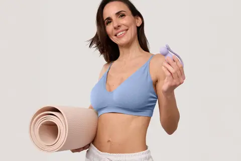Femme souriante tenant un rouleau de tapis et un accessoire pour muscler son périnée.