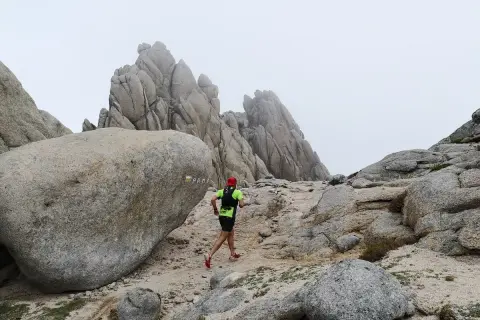 Un coureur en tenue de trail suit le sentier balisé PR-M1, traversant un paysage rocheux et brumeux.