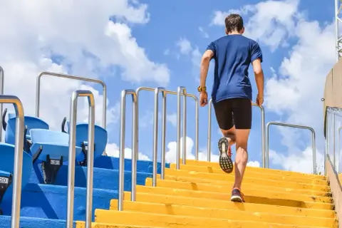 Un homme monte des marches jaunes, un entraînement efficace pour les meilleurs exercices pour les jambes. Le ciel bleu et les nuages sont visibles.