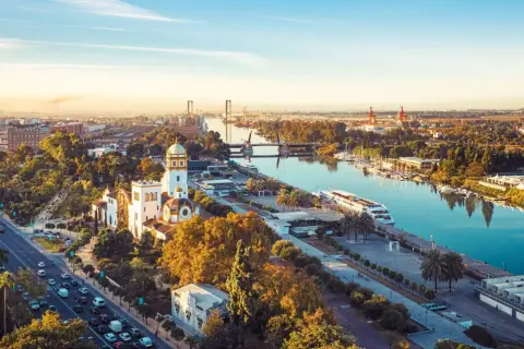 Vue aérienne de Séville au coucher du soleil, avec le Guadalquivir et des bâtiments historiques. Imaginez les coureurs du marathon de Séville 2026 traversant ce paysage.