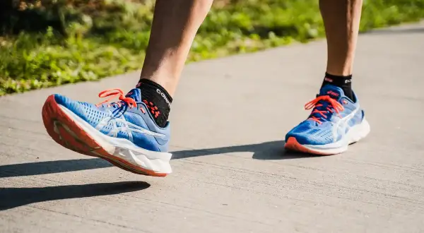Course à pied avec des chaussures bleues et oranges. Le pied gauche montre une légère pronation, typique d'une foulée naturelle.