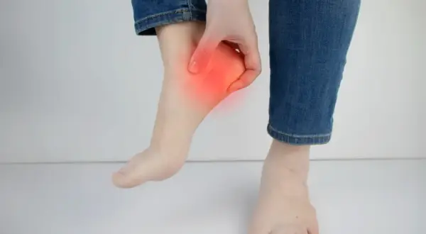 Main d'une personne touchant son talon, zone rouge indiquant une douleur. Peut-être une douleur talon course à pied.