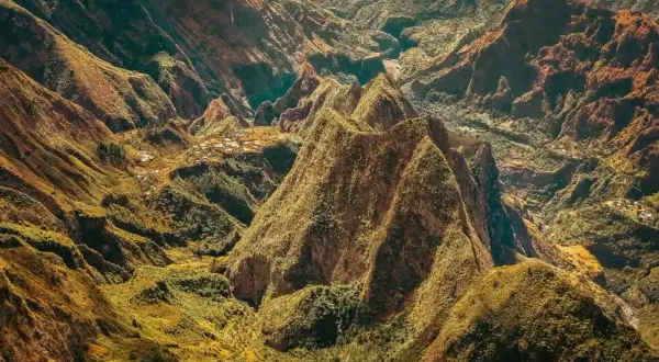 Paysage spectaculaire de montagnes verdoyantes et escarpées, rappelant les défis de la diagonale des fous. Des villages sont nichés dans les vallées.