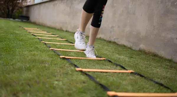 Une personne effectue un exercice lombaire sur une échelle d'agilité dans l'herbe.