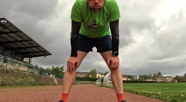 Un coureur fatigué, penché en avant sur une piste d'athlétisme, se prépare pour la récupération course à pied. Le ciel est couvert.