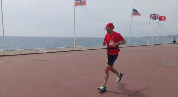 Un homme court sur la promenade des Anglais à Nice, drapeau norvégien et américain en arrière-plan.