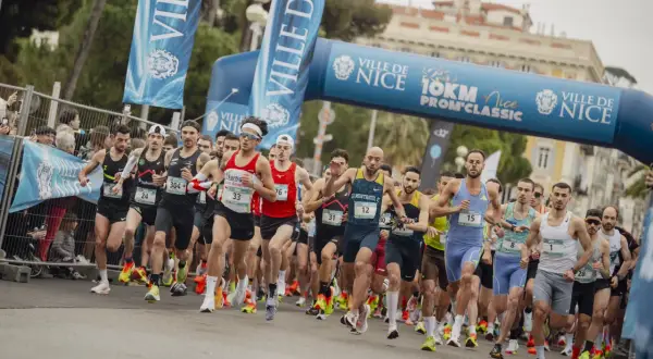 Des coureurs s'élancent sous une arche bleue lors du semi-marathon de Nice. Les numéros de dossard sont visibles.