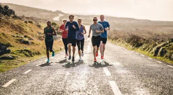 Groupe de coureurs sur une route de campagne ensoleillée. Ils s'entraînent pour comment progresser en course à pied.