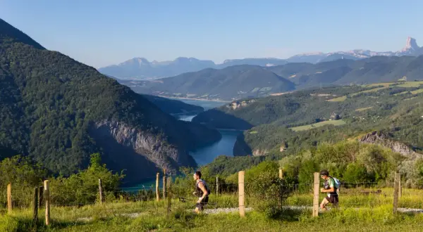 Deux coureurs s'élancent sur le sentier du maratrail des passerelles, dominant un lac bleu entouré de montagnes verdoyantes.