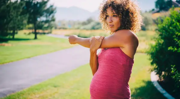 Femme enceinte s'étirant sur un sentier, se demandant si elle peut courir enceinte.