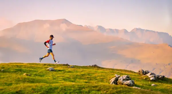 Un coureur en plein effort sur un sentier de montagne, profitant d'un paysage spectaculaire au lever du soleil.