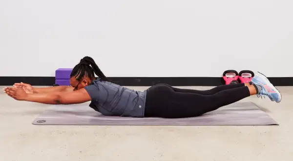 Femme effectuant un exercice abdos au sol, bras tendus devant, jambes levées.