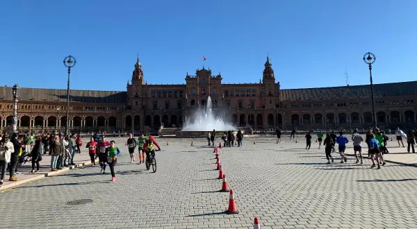 Coureurs et cyclistes s'élancent sur la Plaza de España pour le semi marathon de Séville, sous un ciel bleu éclatant.
