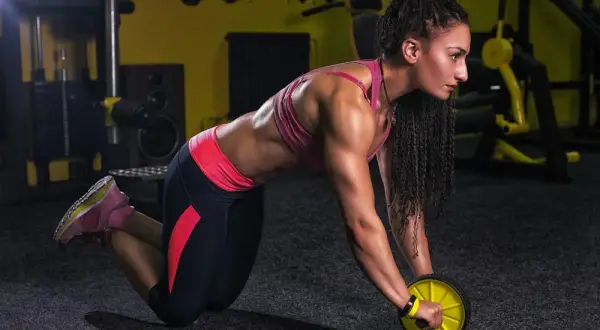 Femme musclée en plein **exercice roue abdominale** dans une salle de sport.