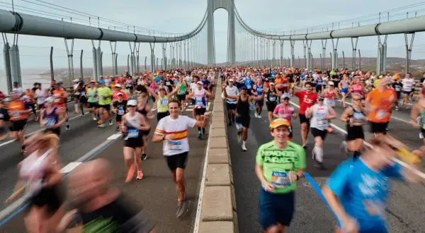 Des coureurs franchissent le pont, affrontant le dénivelé du marathon de New York. Le ciel est couvert, mais l'énergie est palpable.