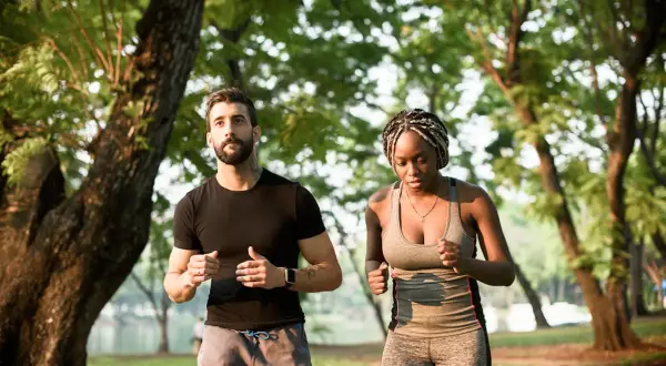 Un homme et une femme courent dans un parc, s'entraînant pour le marathon d'Annecy et son dénivelé.