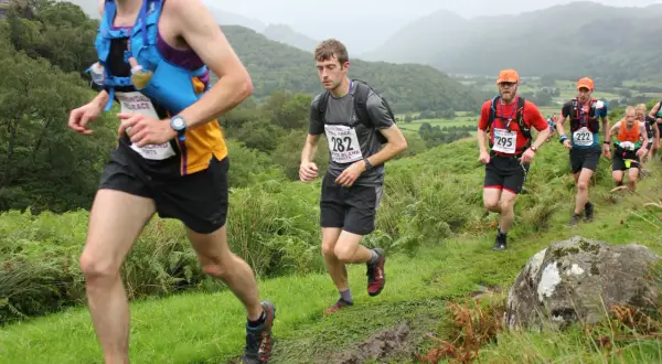 Coureurs en pleine course sur un sentier boueux, dans le cadre du trail des rois maudits. Paysage vallonné et brumeux.