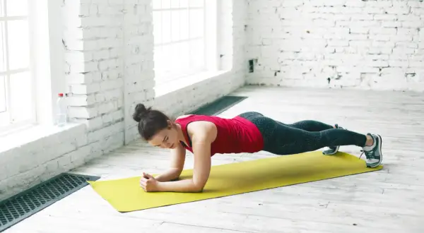 Femme en tenue de sport effectuant la planche sur un tapis jaune, renforçant son corps.