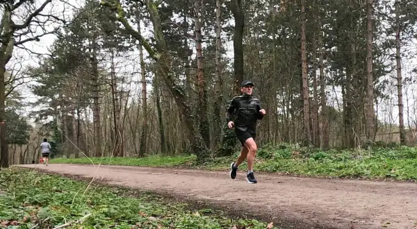 Un homme en tenue de sport ef running sur un sentier forestier, entouré d'arbres.