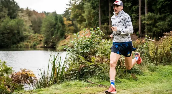 Un athlète court près d'un lac, dans une forêt. Il pourrait s'entraîner pour courir à Nantes.