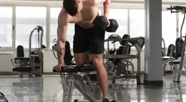 Un homme musclé effectue un exercice haltère, concentré sur son entraînement dans une salle de sport lumineuse.