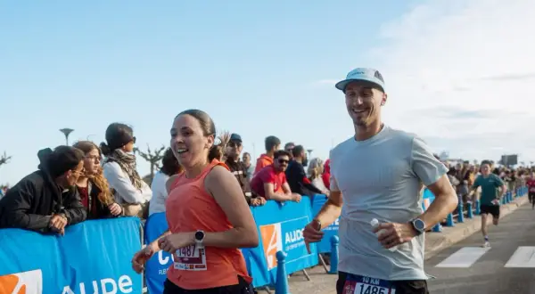 Un couple court joyeusement lors d'un marathon, le soleil brille sur la côte indigo.