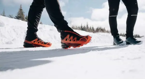 Deux personnes en chaussures de trail, l'une avec des chaussures orange vif, parcourent un sentier enneigé du Haut Giffre.