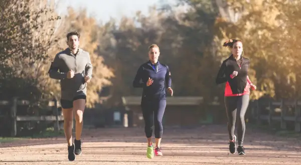 Trois coureurs s'entraînent pour un marathon, profitant d'une journée ensoleillée dans un parc.