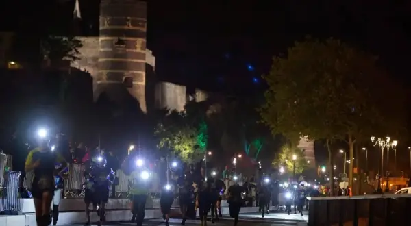 Courseurs illuminés par des lampes frontales, traversant la ville pour le trail de l'apocalypse, avec un château en arrière-plan.