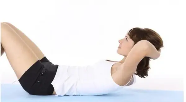 Femme effectuant des abdos hypopressifs sur un tapis bleu.