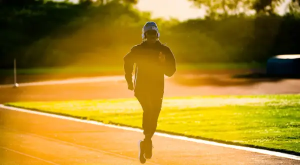 Un jeune homme court sur une piste d'athlétisme à Lyon, baigné par la lumière dorée du soleil couchant.