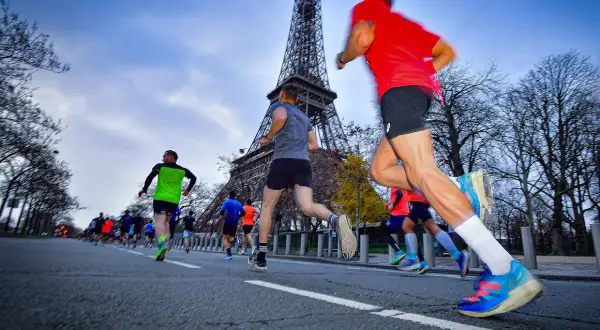 Course de 10 km tour Eiffel, des coureurs en tenue de sport dévalent la route, le monument parisien en arrière-plan.