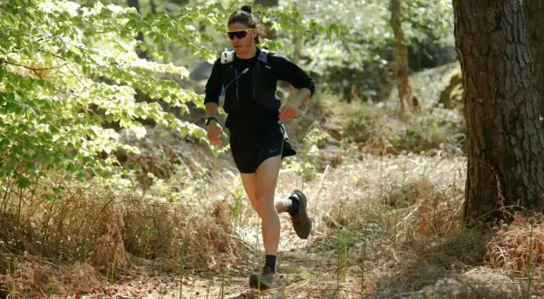 Un coureur s'entraîne dans une forêt ensoleillée, prêt à courir avant une course.