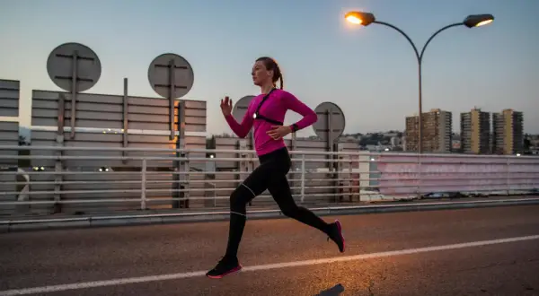Une femme en tenue de sport rose et noire court sur une route au crépuscule, profitant d'une course de nuit sous les lampadaires.