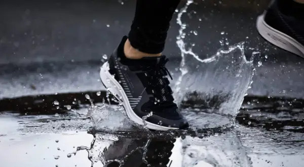Un pied en basket noir et blanc éclabousse l'eau en courant sous la pluie.