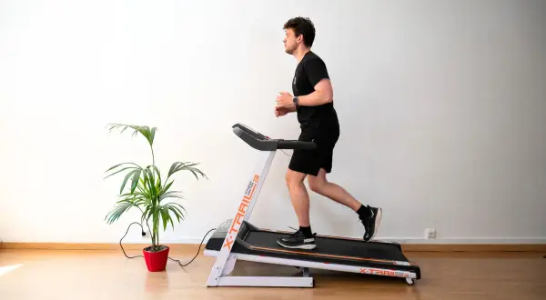 Un homme court sur un tapis de course, suivant un programme d'entraînement. Une plante verte décore la pièce.
