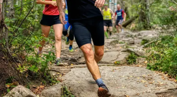 Des coureurs s'élancent sur un sentier rocailleux en pleine forêt. Leurs jambes en pleine action montrent l'effort du running et du jogging.
