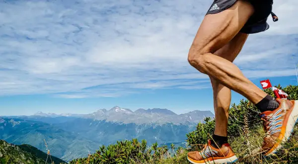 Un coureur en plein entrainement trail, jambes musclées, sur un sentier de montagne avec un panorama spectaculaire.
