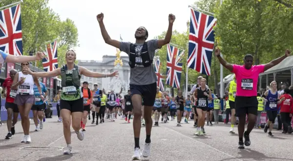 Des coureurs célèbrent leur arrivée au plus grand marathon du monde, drapeaux britanniques en arrière-plan.
