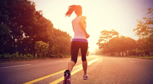 Une coureuse en plein entraînement fartlek, variant son allure sur une route bordée d'arbres au lever du soleil.