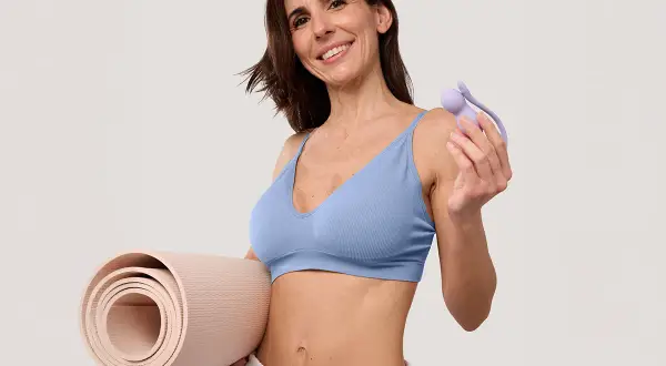 Femme souriante tenant un rouleau de tapis et un accessoire pour muscler son périnée.