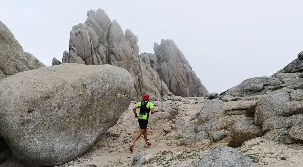 Un coureur en tenue de trail suit le sentier balisé PR-M1, traversant un paysage rocheux et brumeux.