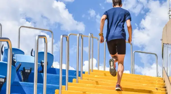 Un homme monte des marches jaunes, un entraînement efficace pour les meilleurs exercices pour les jambes. Le ciel bleu et les nuages sont visibles.